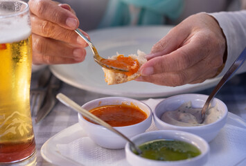 Focus on the hands of a Caucasian woman enjoying the food at the restaurant table tasting the three typical sauces of the Canary Islands, called 