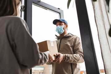 Fototapeta na wymiar health protection, safety and pandemic concept - delivery man in face protective mask giving parcel box to female customer at home