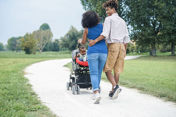 Happy black family having fun walking with stroller outdoor at city park - Focus on kid face