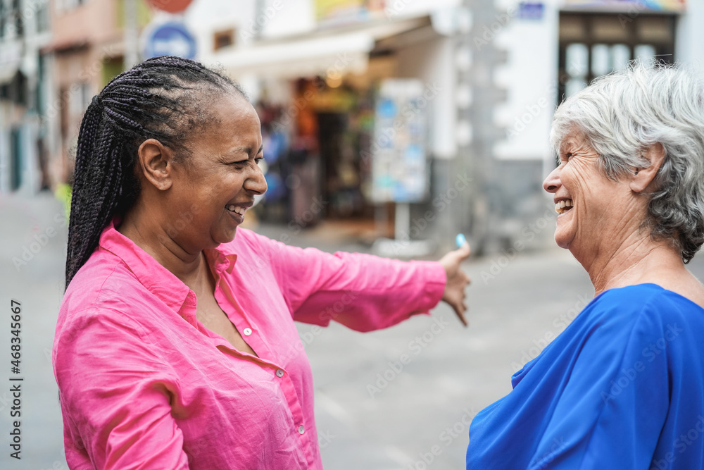 Wall mural senior multiracial women meeting and hugging each others outdoor - focus on african female face