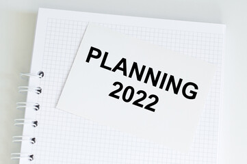 Planning 2022 on a card against the background of a white blaknot on the table, a light soft background, a business concept