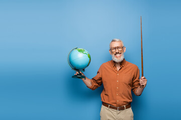 cheerful middle aged teacher in glasses holding pointer stick and globe on blue