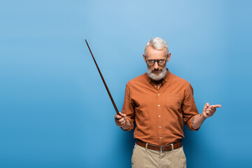 tattooed middle aged teacher in glasses holding pointer stick and pointing away on blue