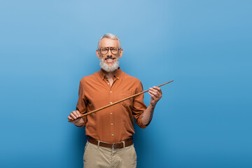 cheerful middle aged teacher in glasses holding pointer stick on blue