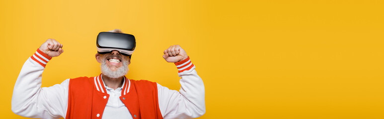 middle aged man in bomber jacket and vr headset rejoicing isolated on yellow, banner