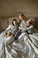 Fototapeta na wymiar Happy family of mom, daughter and son hug joyfully on the bed in the early morning.