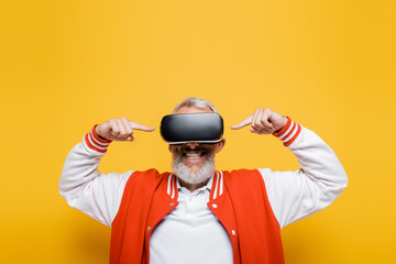 happy middle aged man in bomber jacket pointing at vr headset on yellow