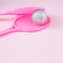 Pink rackets holding Christmas bauble on pink background. Minimal tennis concept.