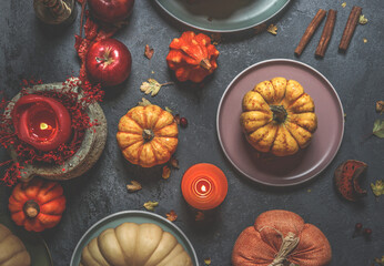 Various colorful pumpkins, candles, plates, cutlery and decoration on dark concrete kitchen table. Rustic autumn still life with seasonal vegetables. Top view.