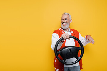 happy middle aged man in bomber jacket holding steering wheel while gesturing isolated on yellow