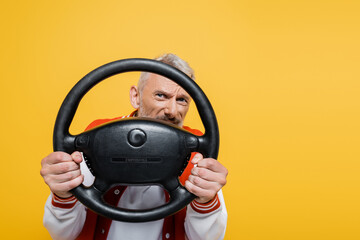 playful middle aged man in bomber jacket holding steering wheel isolated on yellow - Powered by Adobe
