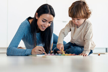 Young beautiful mother painting with her son on the floor in living room at home.