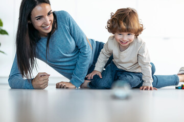 Young beautiful mother playing and having fun on the floor with her son in living room at home.