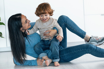 Young beautiful mother playing and having fun on the floor with her son in living room at home.