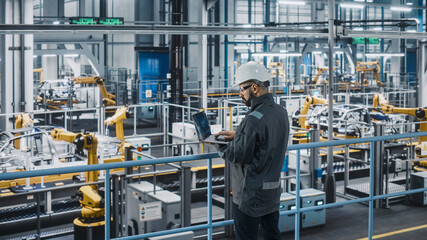 Car Factory Engineer in Work Uniform Using Laptop Computer. Automotive Industrial Manufacturing...