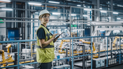 Female Car Factory Engineer in High Visibility Vest Using Laptop Computer. Automotive Industrial...