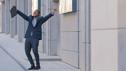Overjoyed confident African businessman winner walk alone outdoors feel overjoyed excited jumping...