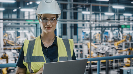 Portrait of Female Automotive Industry 4.0 Engineer in Safety Uniform Using Laptop at Car Factory...