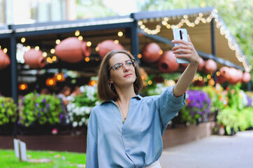 Urban portrait of young attractive business woman in eye glasses and casual clothes. Woman walking in the city street, park, talking on her phone, making selfie, works in sunny day.