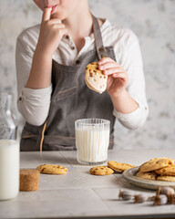 Butter cookies on white table, little child hand soaking biscuit in a milk glass with drops.  Closeup food. Homemade freshly baked dessert with chocolate and caramel. American breakfast. Copy space.