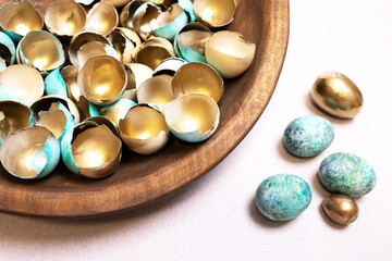 A festive Easter background with lots of golden eggshells and beautiful, modernly colored eggs. Golden eggs as a concept of wealth and success. An original idea for handmade Easter decor. Copy space.