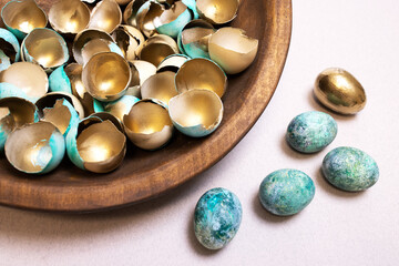Festive Easter background with lots of golden eggshells on wooden platter, beautiful dyed eggs in green and blue. Golden eggs as concept of success, luxury. Original idea for Easter decor. Nobody.