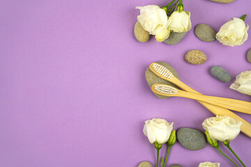 Obraz na płótnie Canvas Natural bamboo toothbrushes with pebbles and flowers on a purple background. No waste concept, no plastic. Copy space