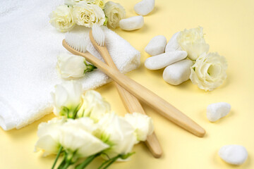 Fototapeta na wymiar Natural bamboo toothbrushes on a towel next to white stone with a flower on yellow background. The concept of zero waste, no plastic