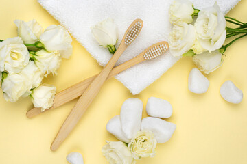 Bamboo toothbrushes with natural white bristles on a towel next to pebbles with a flower on yellow background. The concept of zero waste, modern trends in conscious consumption.