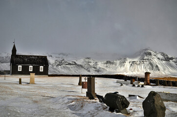 black church in Budir stone fence and in the background snow-capped and misty mountains, Iceland