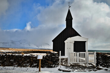 black church in Budir stone fence and in the background snow-capped and misty mountains, Iceland