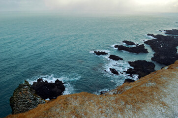 cliff edge and black basalt rocks in the blue sea with fog in the background, Lóndrangar, Iceland
