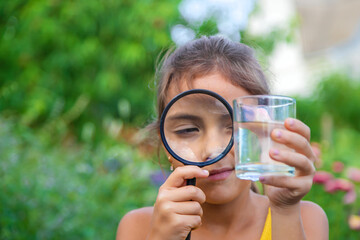 The child examines a glass of water with a magnifying glass. Selective focus.