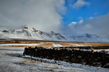 stone fence and in the background snow-capped and misty mountains in Budir, Iceland