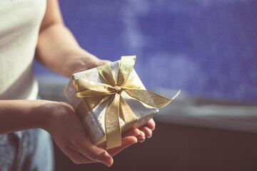 Close up shot of Female hands holding gift box. Copyspace. Christmas, hew year, birthday concept. Festive background with bokeh and sunlight. Magic fairy tale. Shallow depth of field with focus on box