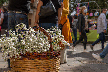 Close-up of some white flowers of the plant Gypsophila paniculata, in a wicker basket. In the background a street market with people out of focus