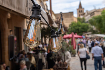 Close-up of a light bulb on the terrace of a restaurant on a shopping street full of people, out of focus