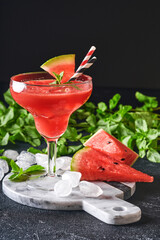 Glass of watermelon Margarita cocktail with mint and ice. Summer refreshing drinks in glasses on black table. Concept of healthy summer eating.