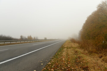Fototapeta premium Asphalt deserted road in fog and autumn landscape along the road.