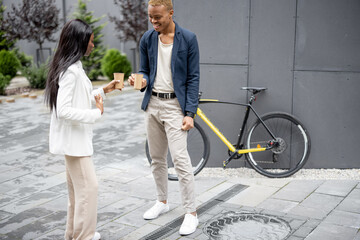 Businessman and businesswoman talking and drinking coffee outdoors. Concept of break on job. Idea of business cooperation. Smiling young man and woman on city street