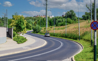 Fototapeta na wymiar winding asphalt road along which a passenger car with bicycles rides, summer cityscape with blue sky and motorway