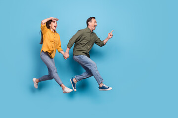 Fototapeta na wymiar Full size photo of brunette haired husband wife amazed jump run empty space point finger isolated on blue color background
