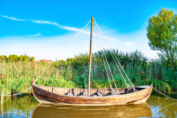 Naklejka na ściany i meble Old wooden boat on lake. Wood rowboat moored near shore