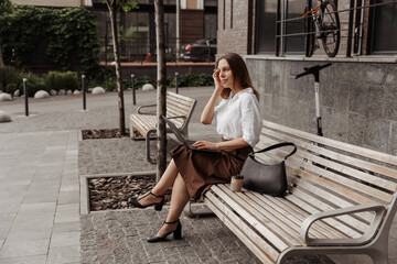 Young business woman sitting on a bench with a laptop of the modern office building background 