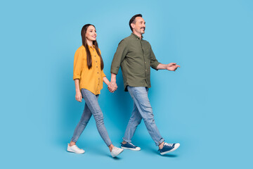 Full size photo of mature positive cheerful man and woman hold hands walk look empty space isolated on blue color background