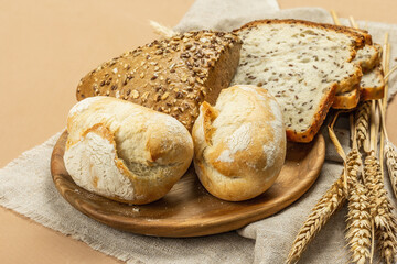 Freshly baked bread with wheat ears, buns, and toasts. Assorted bakery on light beige background