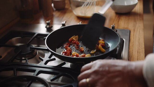 Close up of hands, elderly multi-cultural couple frying vegetables in a pan on the stove in kitchen