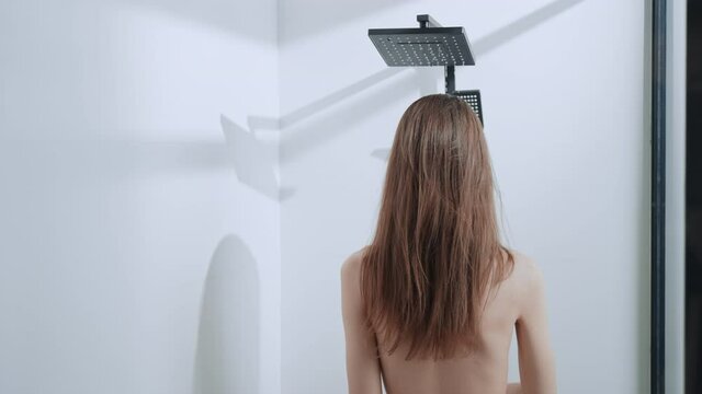 rear view caucasian woman with long hair come in showering cabin bath at home