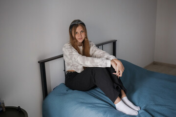 A young 20s girl with a bandage on her head and long blond hair sits in her bedroom on the bed and...
