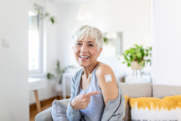 Woman pointing at her arm with a bandage after receiving the covid-19 vaccine. Mature woman showing...